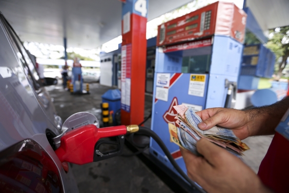 Frentista contando dinheiro em frente a uma bomba de gasolina