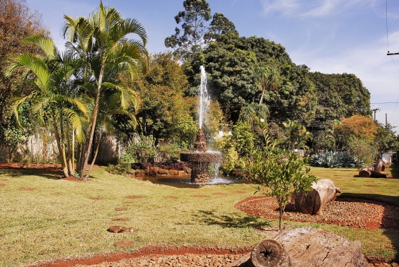 fonte de água dentro de parque, com gramado e árvores verdes ao fundo