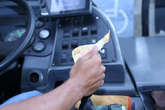 Motoristas segura o volante e uma nota de 20 reais