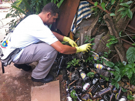 Agente de Combate a Endemias (ACE) retira água parada de garrafas de vidro abandonadas