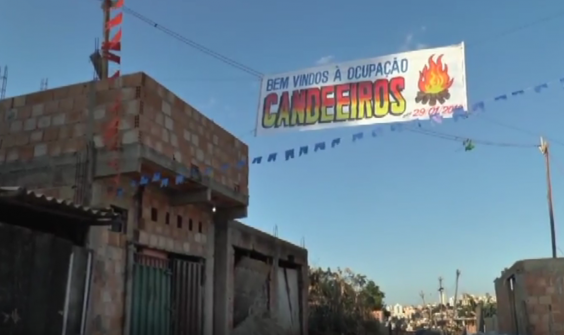 Imagem mostra algumas moradias populares e uma faixa escrito "Bem vindos à Ocupação Candeeiro"
