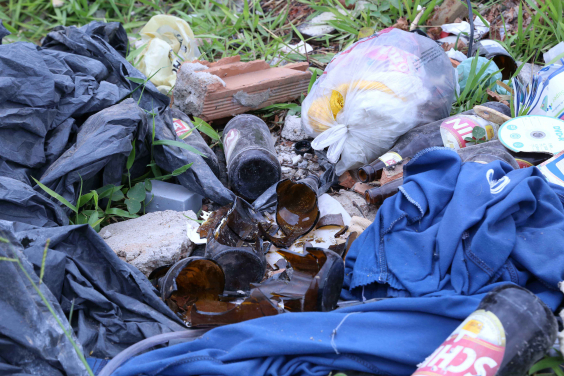 lixo acumulado sobre terreno vago. Garrafas quebradas, roupas, tijolos quebrados e resíduos orgânicos
