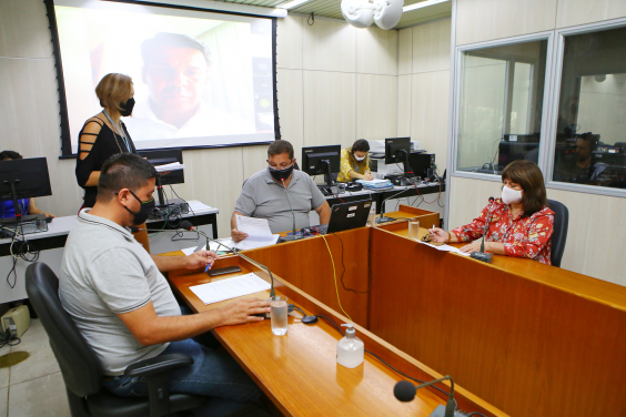 Parlamentares compõem mesa de reunião. Telão ao fundo em videoconferência com os demais membros