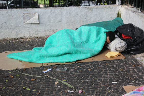 homem dormindo na rua coberto com uma manta verde