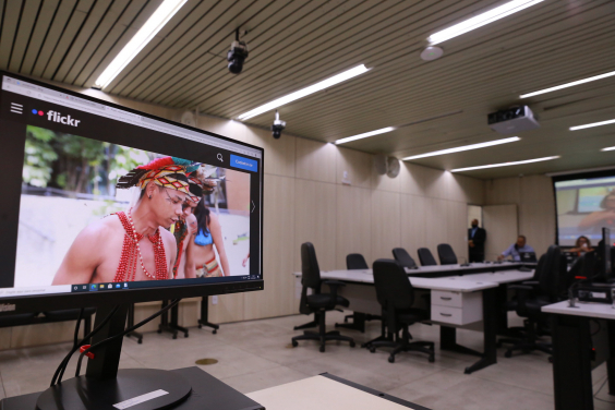 em primeiro plano,  tela de computador mostra indígenas no Plenário Helvécio Arantes