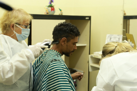 Duas profissionais de saúde com máscara oferecem cuidados a um homem, uma delas corta o cabelo dele. Visita técnica da Comissão de Saúde ao CERSAM - Leste