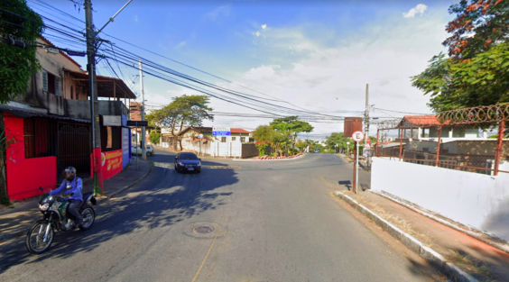 Confluência de quatro ruas, com uma moto e um carro trafegando, durante o dia.