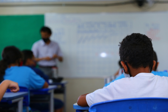 Criança, se costas e de máscara, afastada das outras. crianças, assiste à aula