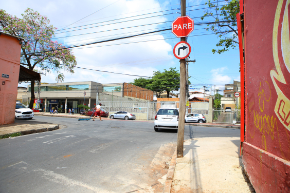 Imagem de um cruzamento de vias com a sinalização horizontal apagada. A sinalização vertical indica parada obrigatória