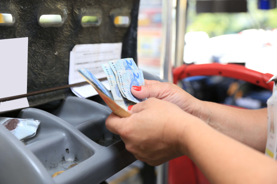 Com as duas mãos, uma pessoas conta notas de dois reais na catraca do ônibus