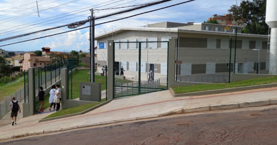 Fachada do Centro de Saúde Havaí, uma casa de dois andares com duas portas e seis janelas frontais, gramas so redor e quatro pessoas atravessando a porta da grade de acesso, durante o dia. 