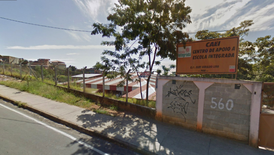 Terreno com grade e muro com placa com os seguintes dizeres: Caei - Centro de Apoio a Escola Integrada. Ao fundo, tenhado de residência, durante o dia.