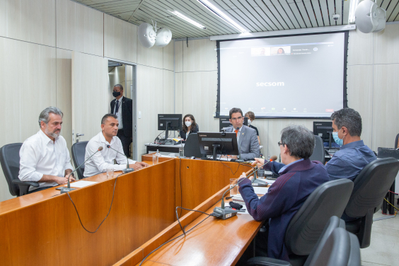 três vereadores e dois cidadão em reunião, sentados à mesa. Ao fundo, um assessor de pé e dois sentados. 