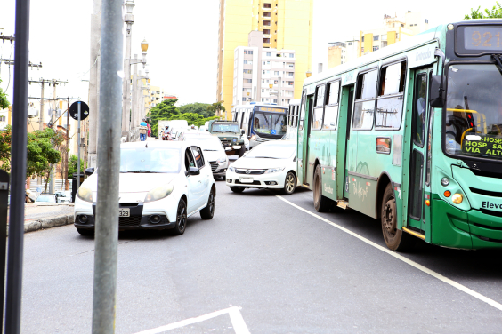 Dois ônibus e três carros à frente de um trânsito cheio de veículos.