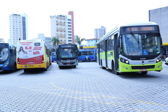 Quatro ônibus coletivos estão estacionados em um pártio