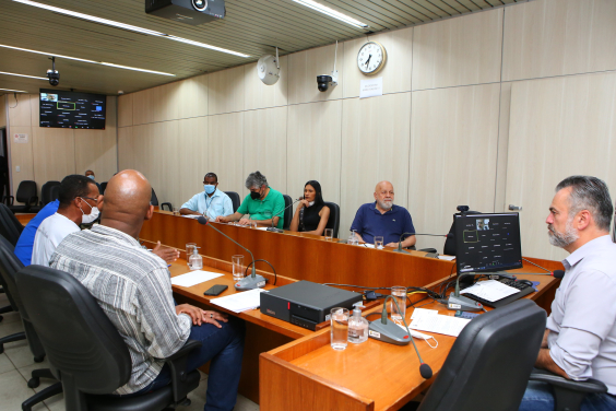 Sete homens e uma mulher reunidos, sentados à mesa.