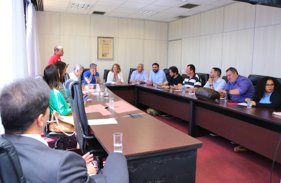 Imagem dos participantes da reunião sentados em uma mesa em formato de U. Na cabeceira da mesa, a presidente Nely Aquino