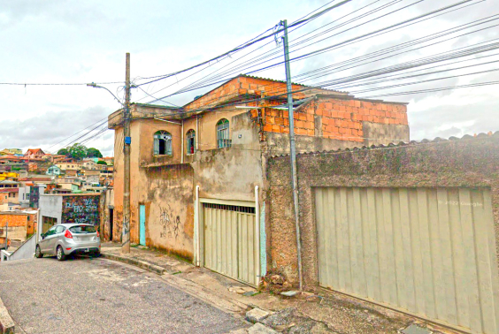 Foto de área residencial com muro e portão seguido de casa de dois andares, durante o dia.