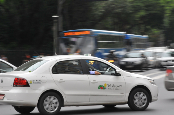 Imagem de um táxi branco em meio ao trânsito da cidade