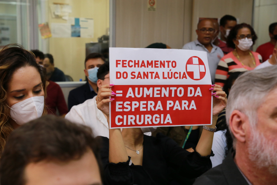 Ao lado de outra mulher, cidadã mostra cartaz com os dizeres: "Fechamento do Santa Lúcia = aumento de espera para cirurgia"