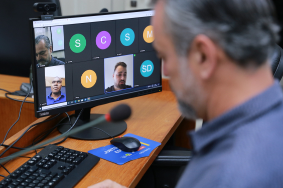 Vereador olha tela de computador que exibe reunião remota com a imagem de dois outros vereadores.