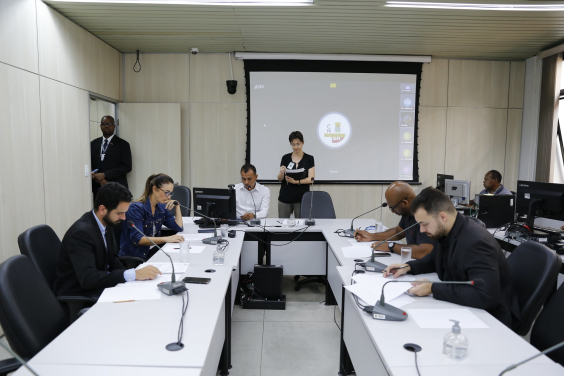 cinco vereadores reunidos, sentados à mesa, acompanhados de três assessores ao fundo.