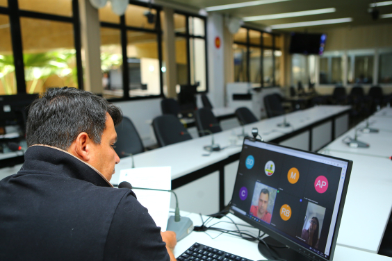 Vereador, sentado em frente ao computador, participa de reunião virtual e olha para tela com a imagem de dois outros parlamentares.
