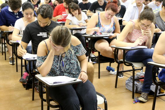 duas fileiras de carteiras escolares, onde candidatos fazem prova de concurso