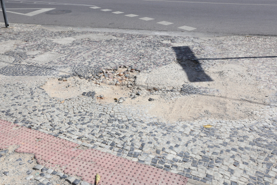 a imagem mostra uma calçada portuguesa com reparo mal feito. é possível identificar o desnível e também terra na parte que deveria estar restaurada
