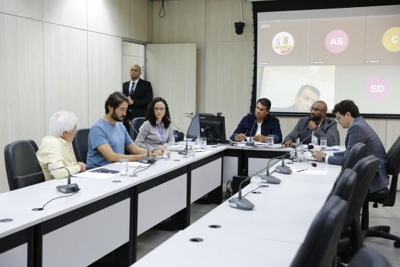 Participantes da reunião sentados em uma mesa em formato de U.