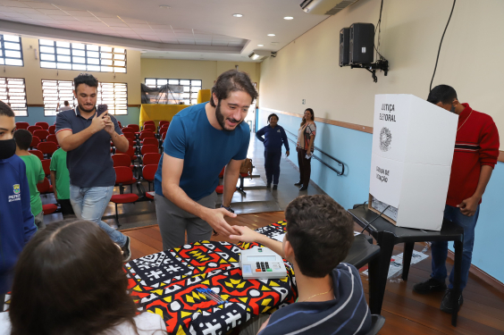 O presidente da CMBH, Gabriel (sem partido) , cumprimenta o mesário. Ao lado, um aluno vota na urna eletrônica do TRE