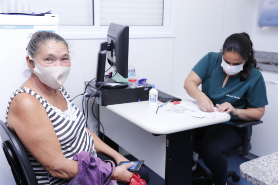 Cidadão, sentada, é atendida por profissional de saúde em consultório