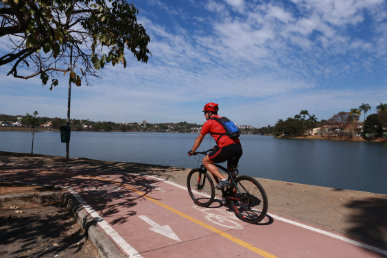 Homem anda de bicicleta em ciclovia da orla da Lagoa da Pampulha, durante o dia. 