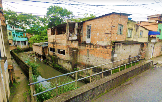 Córrego embiras com lixo em suas águas e rodeado por casas.