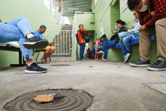 mais de seis pessoas em fila de atendimento em centro de saúde, durante o dia.