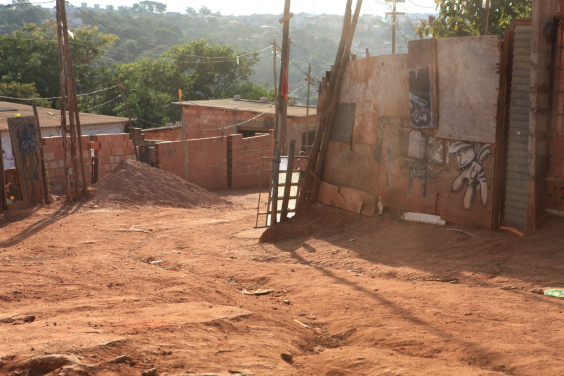 rua sem asfalto rodeada por casas sem reboco, durante o dia.