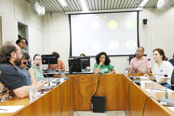 Três mulheres e três homens, sentados, em reunião.