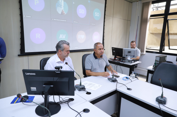 Dois vereadores, sentados à mesa, em reunião presencial