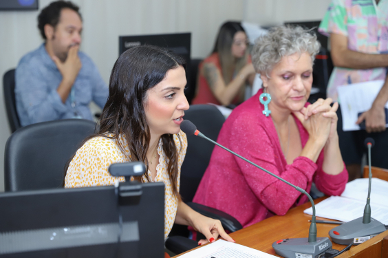 Imagem das vereadoras Marcela Trópia (Novo) e Cida Falabella (Psol) sentadas à mesa , durante reunião da Comissão