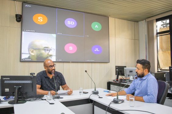 Dois vereadores participam de reunião, sentados à mesa.