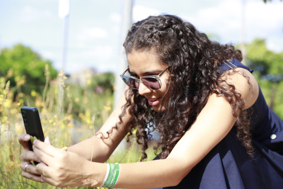 Mulher jovem tira fotos de flores com telefone celular, durante o dia. 