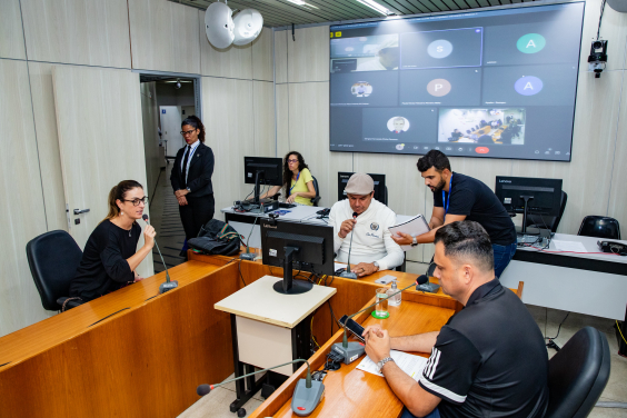 Vereadores discutem projetos no plenário. O telão atrás deles mostra videochamada com vereadores presentes virtualmente.