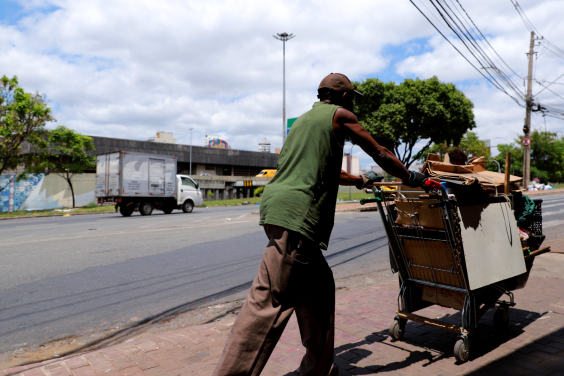 Morador de rua de costas, empurrando carrinho com seus pertences na Praça do Peixe