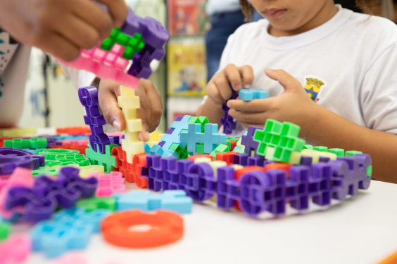 Criança brinca com brinquedos que estão em cima de uma mesa, o rosto dela não é mostrado