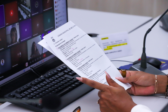 Mãos seguram documento em frente a um computador