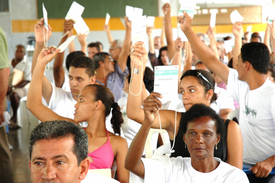 Pessoas erguem uma das mãos segurando fichas brancas em votação