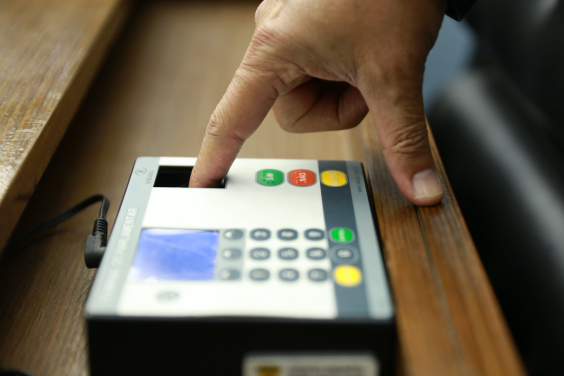 Mão fazendo leitura biométrica de digital em equipamento de votação