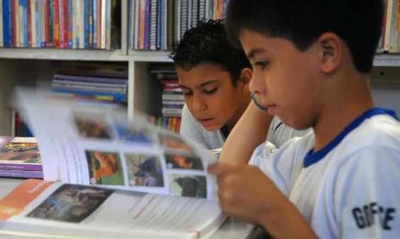 crianças com uniforme de escola fazem leitura de livro em biblioteca