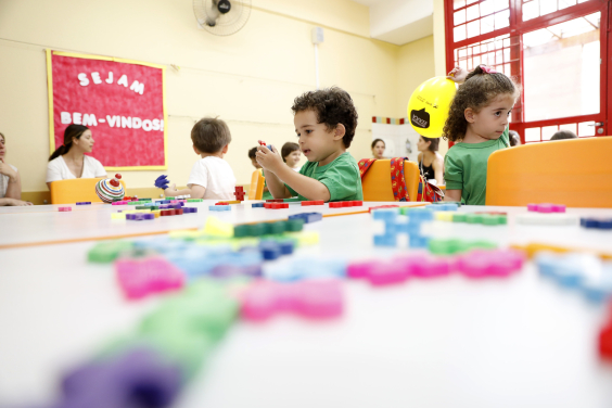 Crianças em sala de aula, com professora ao fundo