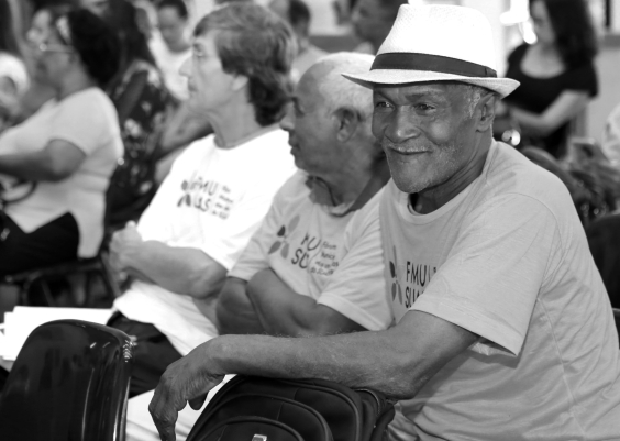 Imagem em preto e branco de três homens idosos sentados lado a lado 